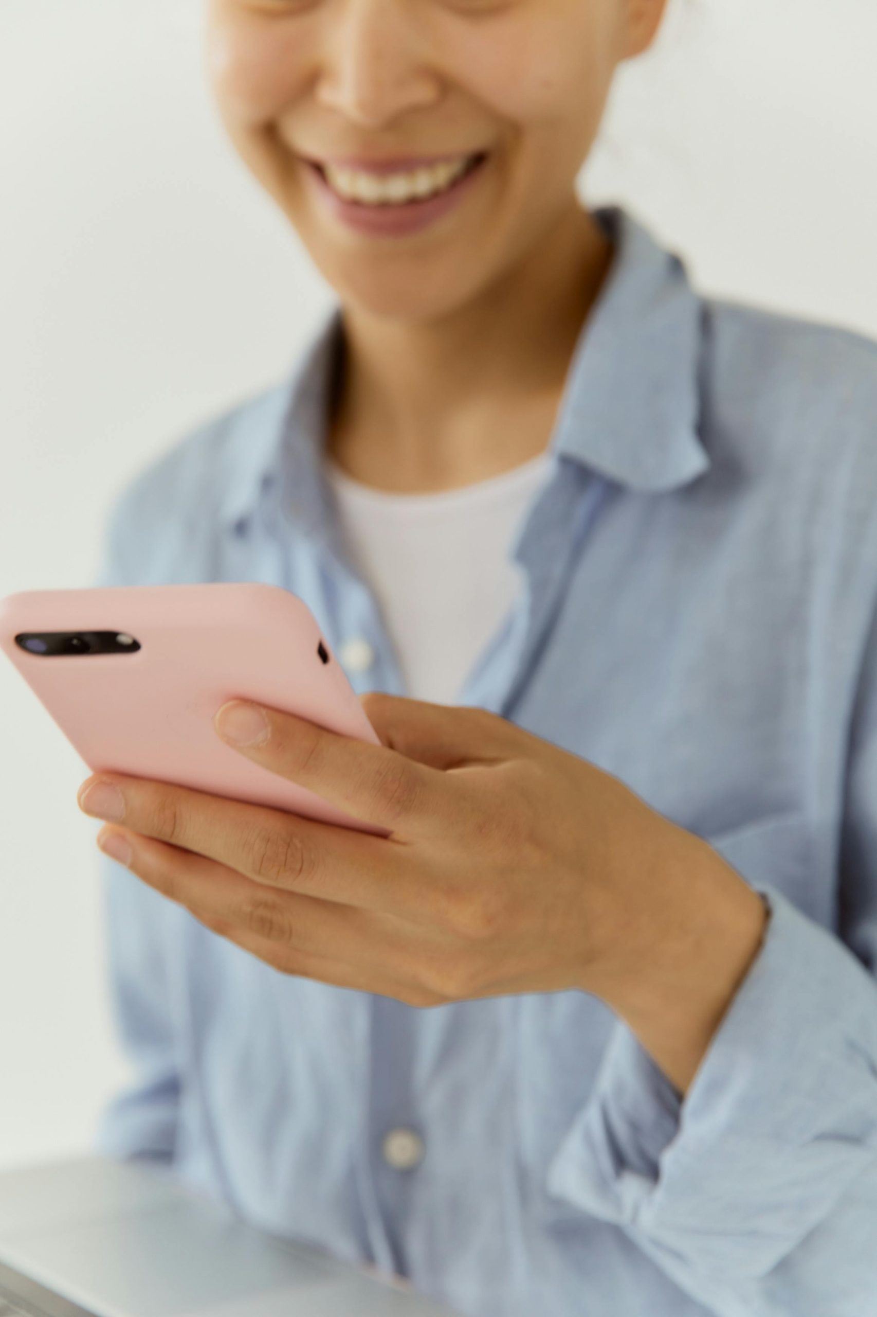 Close-up of a woman smiling while holding a pink smartphone indoors. Casual and friendly atmosphere.